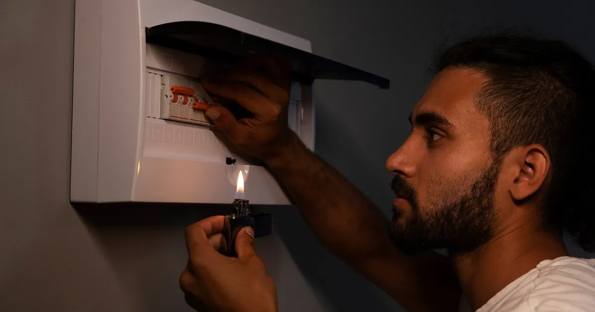 Hombre revisando el cuadro eléctrico de casa con un mechero durante un apagón