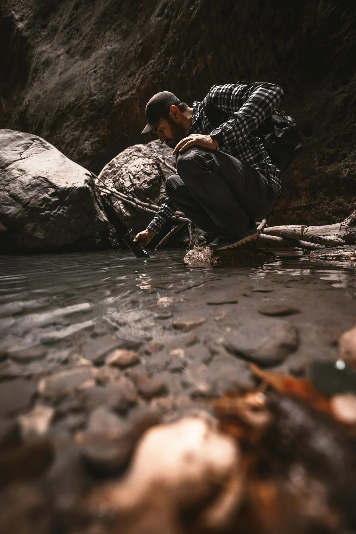Persona usando un filtro de agua portátil para recoger agua directamente de un arroyo de montaña — purificación de agua en emergencias y senderismo