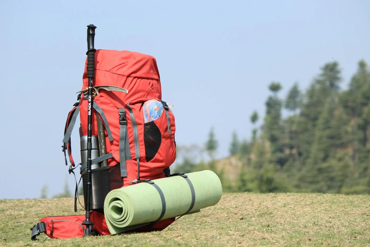 Mochila de senderismo roja sobre hierba con equipamiento de supervivencia: bastón de trekking, esterilla y accesorios — preparación de mochila de 72 horas